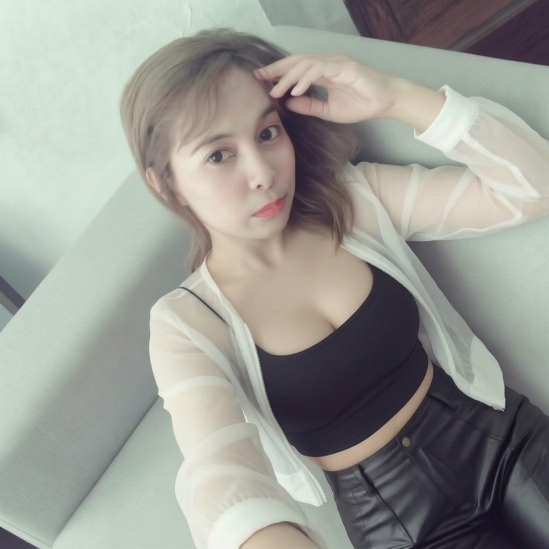 Young woman on a light sofa wearing a black crop top and sheer white jacket, posing for a selfie.