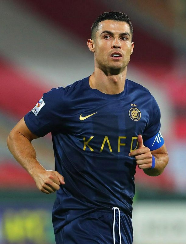 Close-up action shot of Cristiano Ronaldo running mid-match, wearing a navy blue Al Nassr away ki...