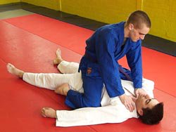 Two people in martial arts gis on a red mat, one pinning the other in a judo/grappling hold.