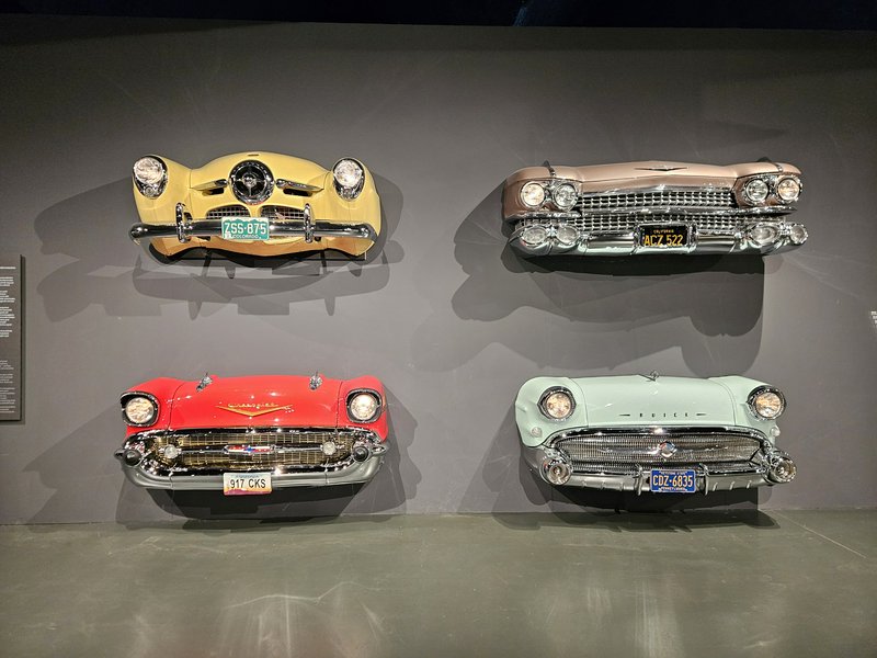Four vintage 1950s American cars mounted as wall art in a museum display.