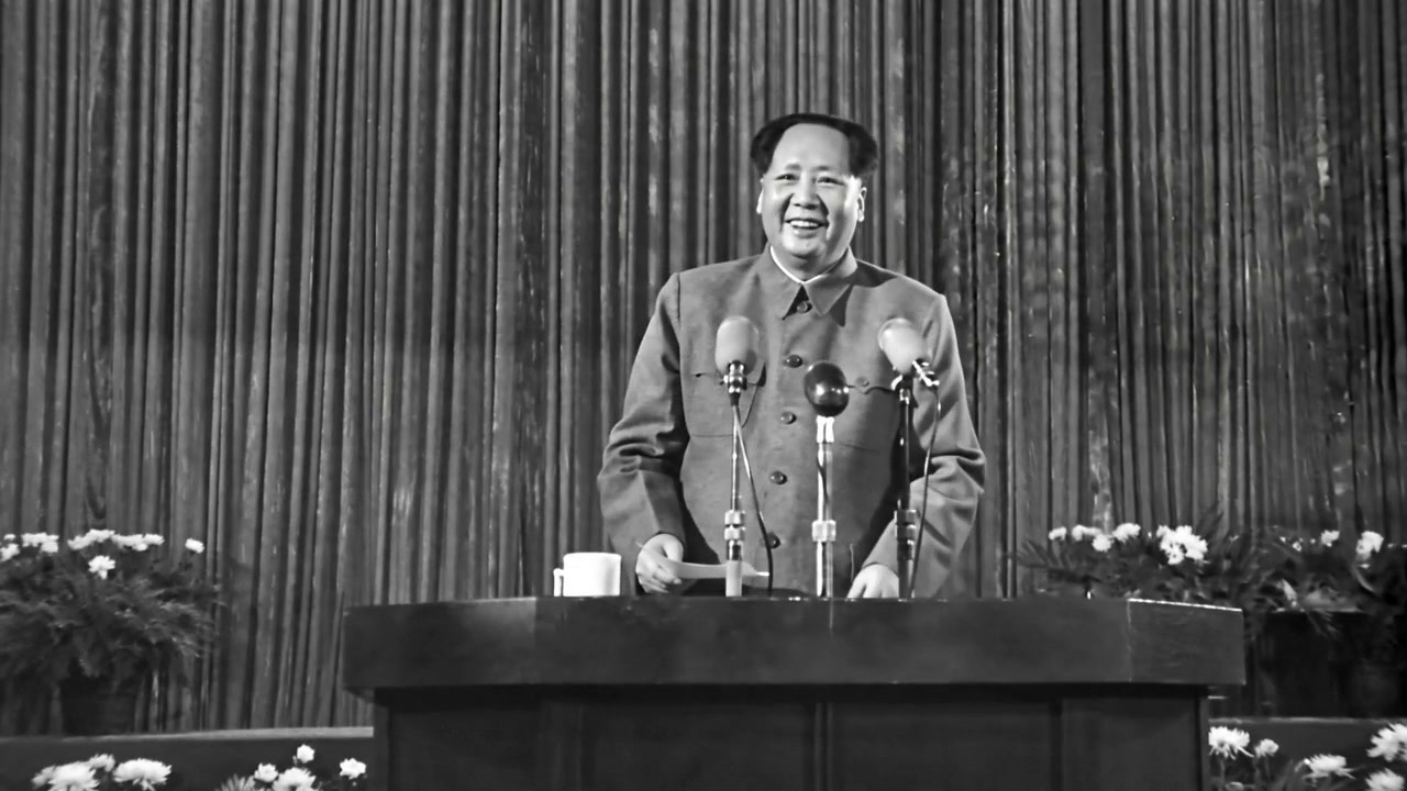 Black-and-white frame of a Chinese political leader at a podium delivering a speech with multiple...