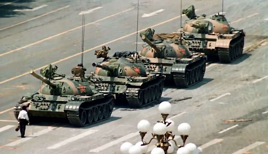 Line of camouflaged tanks with red star insignias rolling down a city street parade.