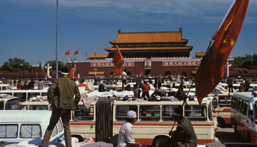 People and vintage buses in front of Tiananmen Gate with red flags on a sunny day.
