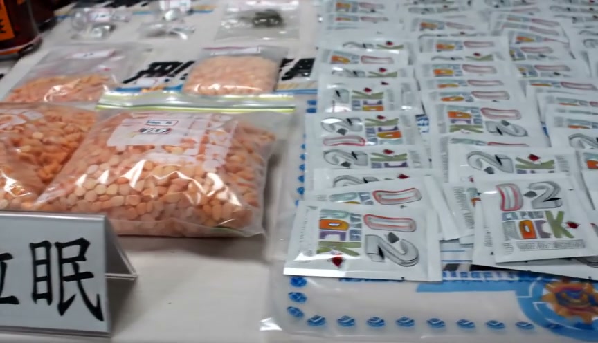 Assorted small orange tablets in bags and numerous labeled sachets on a table, with a sign displa...