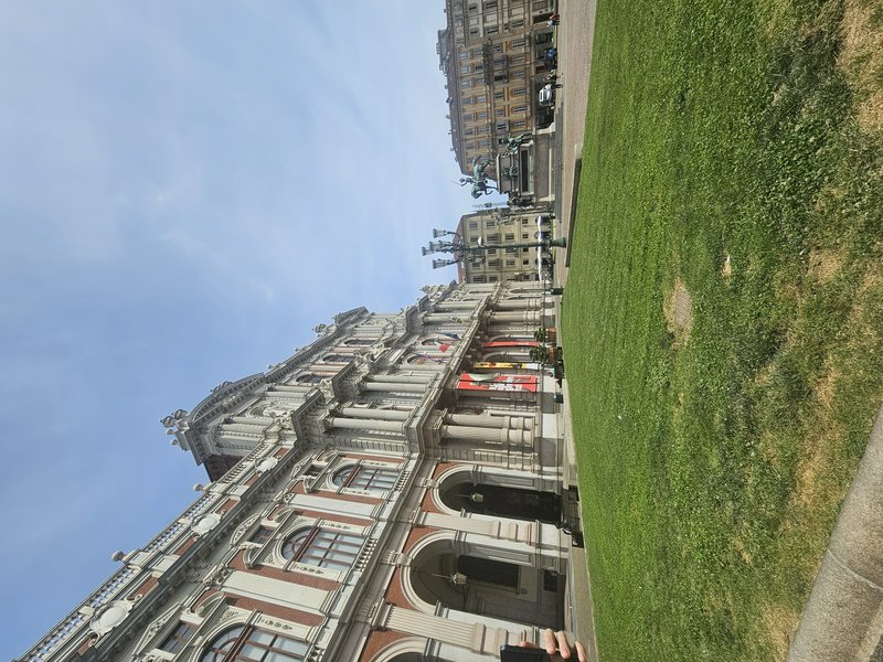 Ornate historic building with arches and columns along a grassy city lawn under a blue sky.