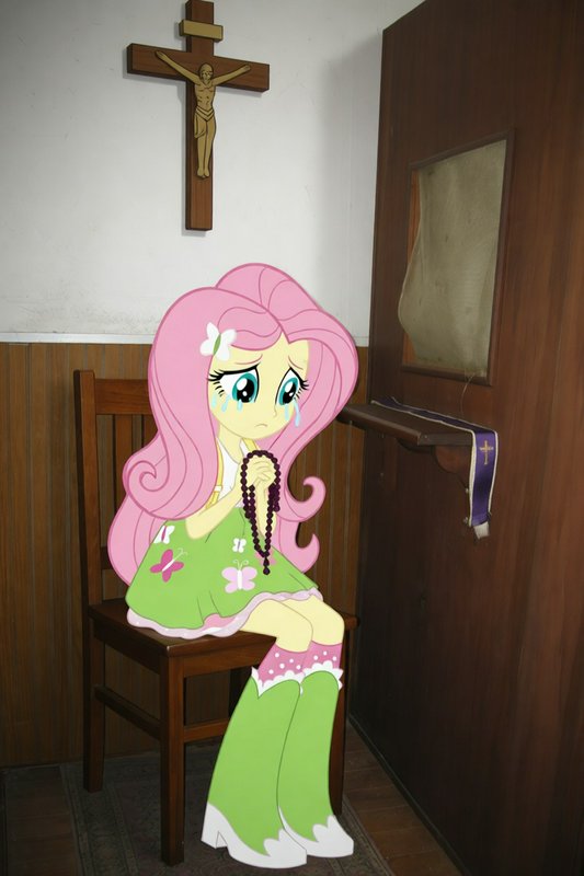 Cartoon cardboard cutout of a pink-haired girl praying with a rosary in a church.